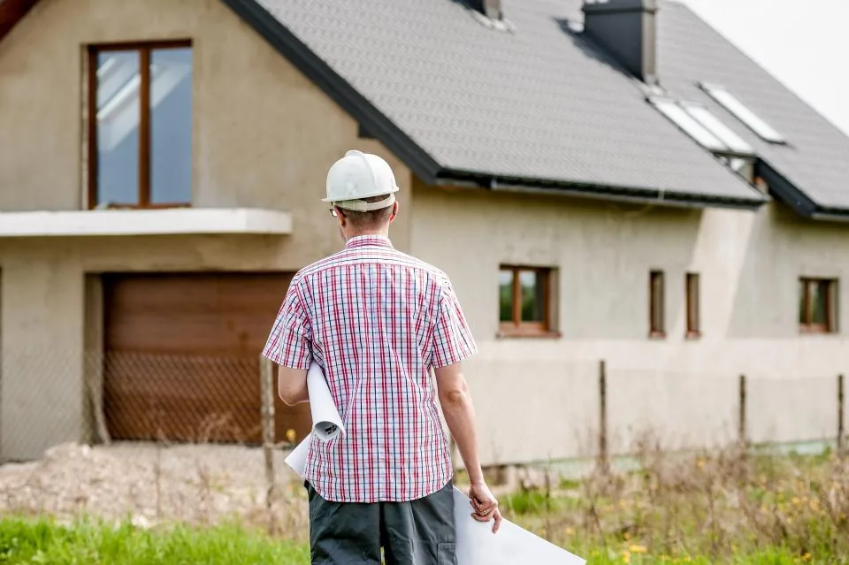 Builder with a hard hat reviewing plans in front of a house