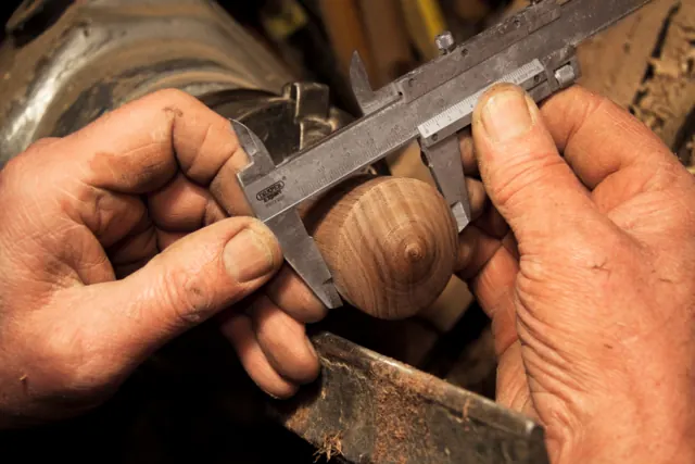 Carpenter measuring a turned wooden part with calipers