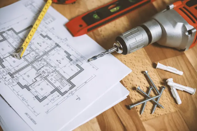 Floor plan, tape measure and drill on a wooden table