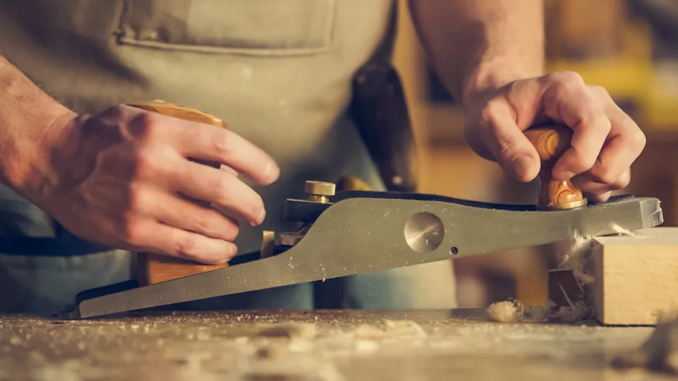 Carpenter shaping a piece of wood with a hand plane